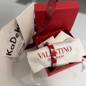 Valentino Garavani armband rött  - Rött valentino armband med guldiga nitar. I mycket fint skick utan defekter eller andra anmärkningar, ej använt mycket. Alla tillbehör medföljer, inklusive kvitto från Kadewe. 