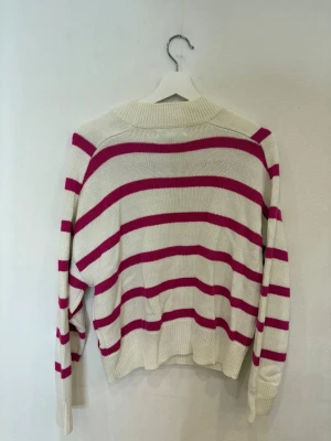 Randig stickad tröja från Amisu - Snygg stickad tröja från Amisu med breda rosa och vita ränder. Modellen har rund hals, ribbade muddar och lång ärm. Perfekt för dig som gillar en chill och färgglad look. Materialet är mjukt och skönt, passar till jeans eller kjol.