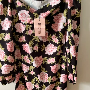 Blommig kortklänning från Missguided - Den är såå fin!!!stk s Supersöt kortklänning från Missguided med svart botten och stora rosa blommor samt gröna blad. Klänningen har långärmade puffärmar och v-ringad hals. Materialet känns lätt och skönt mot huden, perfekt för vår och sommar. Säljer då den inte kommer till användning!