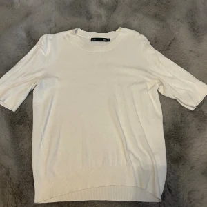 Vit stickad tröja från Lager 175 - Säljer en enkel och stilren vit stickad tröja från Lager 157 med korta ärmar och rund hals. Perfekt för dig som gillar minimalistisk look och mjuka material. Tröjan har ribbade detaljer vid hals, ärmslut och nederkant.