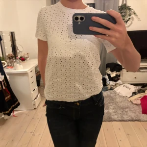 Vit prickig t-shirt i bomull - Säljer en vit t-shirt med korta ärmar och prickigt hålmönster. T-shirten är i mjuk bomull och har en klassisk passform som sitter snyggt på kroppen.