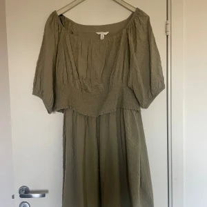 Olivgrön långklänning från H&M Mama - Säljer en olivgrön långklänning från H&M Mama i storlek XL. Klänningen har en lös passform, korta ärmar och smockad midja. Materialet är mjukt och krinklat, vilket ger en chill och avslappnad vibe. Perfekt för dig som gillar enkel stil med lite extra komfort.
