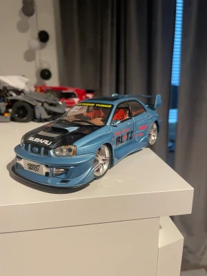 Subaru Impreza WRX STI S202 Extreme Tuner Modellbil - Detaljerad modellbil av Subaru Impreza WRX STI S202 i metallicblått med racingdekor, öppningsbar motorhuv och synlig motordetalj. Utrustad med sportfälgar, stor bakvinge och dekaler. Mycket fint skick, inga synliga skador eller slitage. Kommer med blå ledlight underifrån