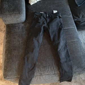Svarta Replay jeans, storlek 14A - Snygga svarta jeans från Replay med klassisk femficksdesign och smal passform. Byxorna har normal midja och raka ben, tillverkade i mjukt jeanstyg som sitter skönt. Perfekta för dig som gillar stilrena och tidlösa jeans.
