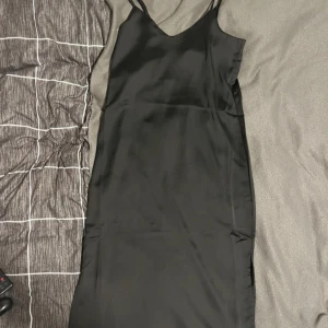 Svart satin långklänning JJXX XS - Svart långklänning från JJXX i glansigt satinmaterial. Klänningen har smala axelband, v-ringad hals och en stilren, slät siluett. Perfekt för dig som gillar minimalistisk och elegant stil. Aldrig använd!