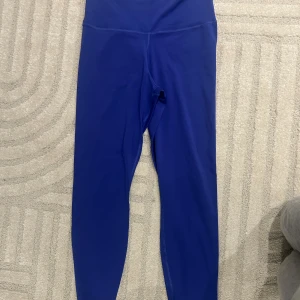 Blå Nike Dri-Fit leggings yoga M - Snygga blå leggings från Nike med Dri-Fit material, perfekta för yoga och träning. Högmidjade med smal passform och diskret Nike-logga framtill. Stretchigt syntetmaterial som andas och sitter skönt under hela passet.