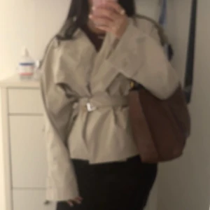 Beige trenchcoat med bälte - Säljer en beige trenchcoat med bälte i midjan och långa ärmar. Jackan har en klassisk omlott-design och är perfekt för dig som gillar stilrena och tidlösa plagg. Passar dig som vill ha en snygg och enkel jacka till vardags. S/m