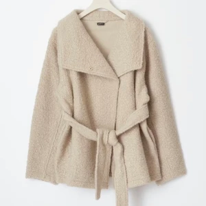 Beige teddyjacka med bälte från Gina Tricot - Supermjuk och oversized teddyjacka i beige från Gina Tricot. Jackan har bred krage, knytbälte i midjan och långa ärmar. Perfekt för lager-på-lager och chill höst- och vinterstil. Enkel knäppning framtill och riktigt cozy material.