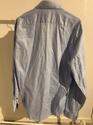 Ljusblå slim fit skjorta Egyptisk bomull - Fräsch ljusblå skjorta från dressmann i slim fit-modell. Skjortan har klassisk krage, svarta knappar och långa ärmar med knappslå. Tillverkad i mjuk och tunn bomull, perfekt för dig som gillar stilren och enkel design.