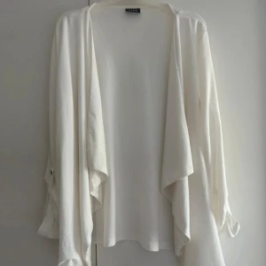 Vit cardigan jacka från Vila - Säljer en vit cardigan jacka från Vila med omlott-design och långa ärmar. Koftan har snygga detaljer med knapp vid ärmslut, vilket ger en chill och flowig vibe. Perfekt för lager-på-lager och passar till många olika stilar