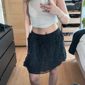 Marinblå kortkjol med vita stjärnor  - Supersöt marinblå kortkjol med vita prickar och lätt volang. Kjolen har resår i midjan för en bekväm passform och är gjord i ett tunt, luftigt material som ger en flowy känsla. Perfekt att styla med en crop top eller stickad tröja. Insydd i midjan 