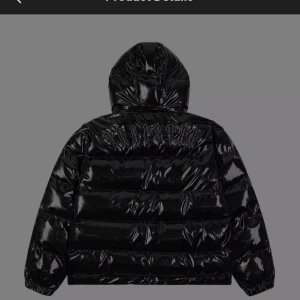 Helt ny svart Trapstar pufferjacka med huva - Svart glansig pufferjacka från Trapstar med broderad logga på ryggen och rund patch med 'T' på bröstet. Jackan har huva, dragkedja framtill och två fickor. Perfekt för dig som vill ha en streetstyle-look med edge.