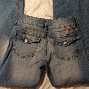 Bootcut Flare Low Waist y2k jeans från Divided H&M - Ett par Low Waist Flared Bootcut Y2K Jeans från Divided (Angelic Denim kollektionen) H&M i storlek 38 (M). 2 Knappar & dragkedja i gylfen, fickor med knapp på bakfickorna. Använda men i gott skick, lite smått smutsiga (har tvättats) & lite veckade och minimala slitningar längst ner, några enstaka lösa trådar (märks inte vid användning). Innerbenslängd: ca 78 cm. Hör av er om ni önskar fler bilder eller annat🌷
