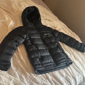 Svart dunjacka Peak Performance 160 - Svart dunjacka från Peak Performance med huva och dragkedja framtill. Jackan har quiltad design och logga på bröstet. Perfekt för kalla dagar, snygg och funktionell med långärmade ärmar och normal passform. säljer pågrund av fel storlek och helt oanvänd.💗