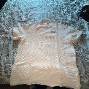 Beige ribbad t-shirt från Bershka - Säljer en beige ribbad t-shirt från Bershka med broderad text 'JOIE DE VIVRE.' på bröstet. T-shirten har korta ärmar och en skön, lite tjockare struktur som ger en cool vibe. Perfekt för dig som gillar stilrena detaljer och fransk touch.