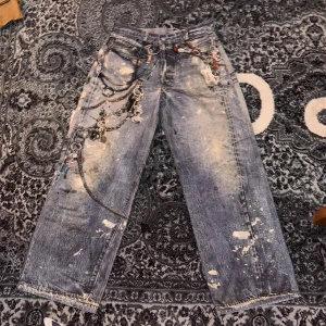Acne Studios digital print - Unika blå jeans från Acne Studios med raka ben, dekorerade med kedjor, nyckelringar och färgstänk. Jeansen har en cool, sliten look och är tillverkade i 100% bomull. Perfekta för dig som vill sticka ut med en edgy streetstyle. Svåra o få tag på