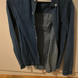 Blå jeansskjorta crocker XS - Säljer en klassisk blå jeansskjorta från Crocker  i storlek XS. Skjortan har långa ärmar, knappar framtill och en snygg krage. 