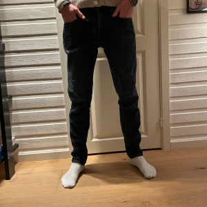 Replay anbass jeans - Snygga svarta jeans med smal passform och klassisk femficksdesign. Jeansen har en mörk tvätt och raka ben med lätt tapered siluett. Perfekta för dig som gillar en stilren look och vill ha ett par jeans som sitter snyggt över benen. Storlek 31/32