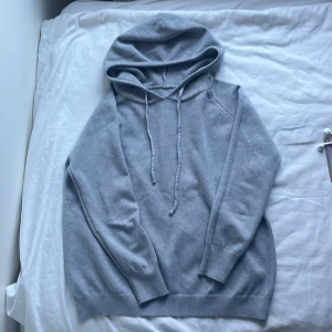 Merino ull Grå hoodie med snörning och huva - En stilren grå hoodie med mjuk känsla och ribbade muddar vid ärmslut och nederkant. Tröjan har en klassisk huva med snörning och långärmade raglanärmar. Perfekt för chill dagar och enkel att matcha med jeans eller joggers. Storlek S (ca 170 cm)