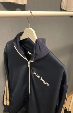 Mörkblå trackjacka från Palm Angels - Säljer en mörkblå trackjacka från Palm Angels med vita detaljer och dragkedja framtill. Storlek M