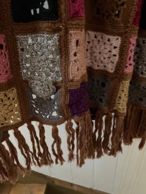 Odd Molly långkofta virkad mormorsrutor - Unik långkofta från Odd Molly, virkad i färgglada rutor med blommiga detaljer och fransar längst ner. Koftan  har lång ärm och är gjord i bomull med inslag av glittertråd. Färgerna är blandade med beige, rosa, lila, röd, svart, grå och guld. Perfekt för dig som gillar boho och virkat. St 1