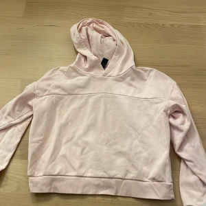 Ljusrosa hoodie från SOC - Snygg ljusrosa hoodie från SOC i mjuk bomullsmix. Tröjan har huva, långa ärmar och ribbad nederkant. Enkel och clean design utan tryck eller mönster, perfekt för chill dagar. Passar dig som gillar en avslappnad stil.