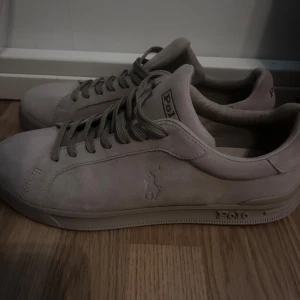 Beige sneakers från Polo Ralph Lauren - Snygga beige sneakers från Polo Ralph Lauren med klassisk låg profil och rund tå. Skorna har mockaöverdrag, snörning och diskret Polo-logga på sidan och sulan. Perfekta för dig som gillar stilrena och neutrala färger. Näst intil helt nya använda en gång. 