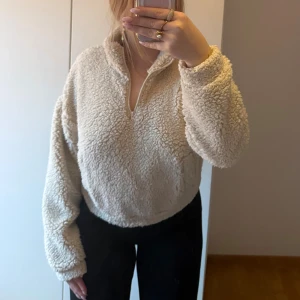 Beige croppad fleece-tröja med half zip - Supermysig beige fleece-tröja från Bik Bok med croppad passform och half zip framtill. Tröjan har långärmade ärmar, hög krage och ett fluffigt, teddy-liknande material. Dragsko nedtill för att justera passformen så man kan ha den lite längre som på första bilden eller croppad som på andra. Använd en gång. 