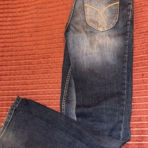Blå jeans med kontrastsömmar - Säljer ett par klassiska blå jeans med snyggt slitna detaljer och kontrastsömmar på bakfickan. Jeansen har rak passform och normal midja, tillverkade i tåligt denimtyg. Perfekta för dig som gillar en tidlös och avslappnad stil.