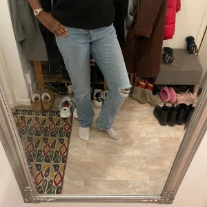 H&M jeans - Säljer ett par ljusblå jeans från H&M i klassisk straight fit med hög midja. Jeansen har en snygg slitning på ena knät. 