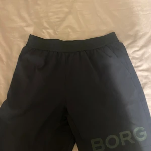 Svarta träningsshorts från Björn Borg - Säljer ett par svarta träningsshorts från Björn Borg i storlek M. De har elastisk midja och en stilren design med loggan 'BORG' tryckt på benet. Perfekta för gymmet eller sport, tillverkade i lätt polyester som andas.