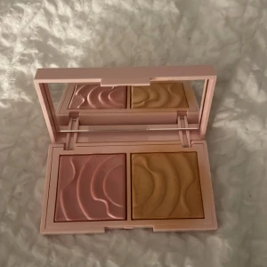 CAIA duo-palett med rouge & highlighter - Säljer en snygg duo-palett från CAIA med ett vågmönstrat rouge i mjuk rosa och en highlighter i varm champagneguld. Kommer i en ljusrosa, stilren ask med spegel i locket – perfekt för att fixa glow och färg på kinderna.