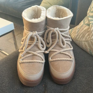 Beige Inuikii  - Säljer ett par helt oanvända beige Inuikii med mjuk pälsfoder och grova snören runt hela skon. Utsidan är i mocka och skinn, med platt brun sula och rund tå. Perfekta för kalla vinterdagar och har en riktigt cozy vibe. 