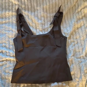 Brun linnetopp med knytband - Snygg brun linnetopp med breda axelband som knyts till rosetter på axlarna. Toppen har en rak och något figurnära passform med slät yta och stilren design. Perfekt för dig som gillar enkla men trendiga plagg med fina detaljer. De storlek L på den men de skulle mer vara M. Jag har aldrig använt den 