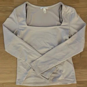 Beige långärmad topp från H&M - Säljer en stilren beige långärmad topp från H&M med fyrkantig urringning. Toppen har en slät och mjuk yta, är figurnära och passar perfekt till jeans eller kjol. Materialet är stretchigt och bekvämt, vilket gör den enkel att bära hela dagen.