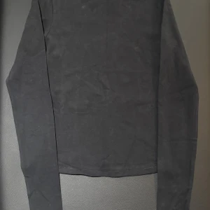 Svart långärmad tröja från SKIMS i storlek XS - En stilren svart långärmad tröja från SKIMS i mjuk bomull. Tröjan har en klassisk rund halsringning och enkel design som funkar till många olika looks. Perfekt för dig som gillar minimalistisk stil och vill ha en basic i garderoben.