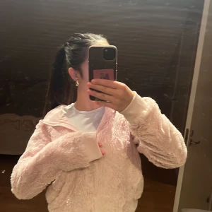 Ljusrosa teddyjacka med huva KappAhl - Supermjuk och fluffig teddyjacka från KappAhl i ljusrosa. Jackan har huva, dragkedja framtill och breda muddar vid ärmsluten. Perfekt för dig som gillar mysiga och trendiga plagg. Passar dig som vill ha en chill och cozy vibe.