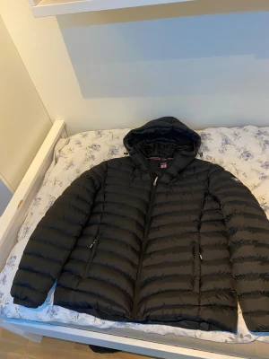 Svart pufferjacka från Vinson Polo Club - Svart pufferjacka från Vinson Polo Club med huva och dragkedja framtill. Jackan har quiltad design med horisontella sömmar och två fickor med dragkedja. Nästan oanvänd, Skriv vid minsta lilla fråga :)