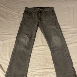 Replay grå jeans straight fit - Snygga grå jeans från Replay med klassisk femficksdesign och raka ben. Jeansen har dragkedja och knappstängning, samt tydliga sömmar och Replay-logga på insidan. Perfekt för dig som gillar stilrena och tidlösa jeans.
