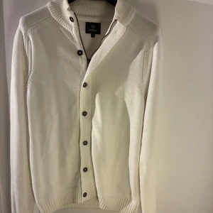 Less Worries – Vit kofta (L) - Säljer en vit kofta från Less Worries i storlek L. Den har både dragkedja och knappar framtill samt en ribbad krage som sitter skönt. Koftan är använd några få gånger och är i bra skick utan skador eller fläckar. Nypris: 799kr.