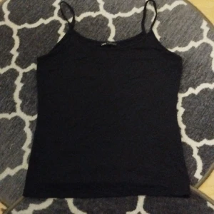 Svart linnetopp från Zara - Enkel och stilren svart linnetopp från Zara med smala axelband. Toppen är figurnära och har en klassisk rak form, perfekt att matcha med jeans eller kjol. Tillverkad i mjuk bomull för en bekväm känsla hela dagen.