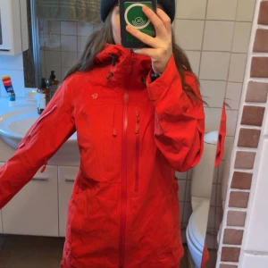 Norrona Jacka - Röd/orange skaljacka från Norrøna. Köpt här på Vinted men passade inte så säljer den! Storlek: XS. Färg: Tasty Red (röd/ orange). Bra skick, tecken på användning finns men inga stora hål eller liknande. Har snölås och flera fickor (inner också).