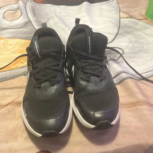 Svarta Nike sneakers strl 38 - Säljer ett par svarta Nike sneakers med vit sula och klassisk swoosh på sidan. Skorna har mesh-överdel för bra ventilation, snörning och rund tå. Perfekta för dig som gillar sportig stil och vill ha bekväma skor till vardags.