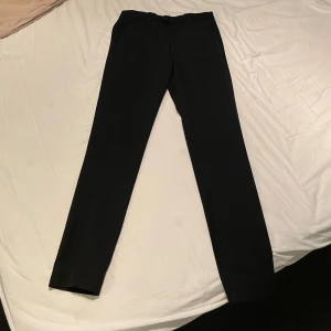 Svarta Jack & Jones chinos - Svarta chinos från Jack & Jones, modell Slim/Marco. De är i storlek 31/34 och nypris ligger på ca 600kr. Byxorna är i stort sett i nyskick, har endast använts några gånger. Hör av er vid eventuella funderingar!