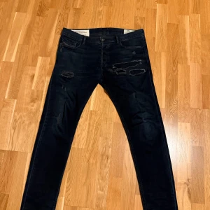 Diesel Tepphar-X svarta slim jeans  - Svarta Diesel Tepphar-X jeans med slim carrot passform. Jeansen har snygga slitningar och stretchigt material för extra komfort. Klassisk femficksdesign och diskret Diesel-logga på bakfickan.  Storlek W33 L32