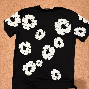 Svart t-shirt med vit blommig print - Svart t-shirt med coola vita blommiga mönster över hela tröjan. Klassisk passform och rund halsringning, perfekt för dig som vill sticka ut med en unik stil. Skön och mjuk känsla, passar till jeans eller shorts.