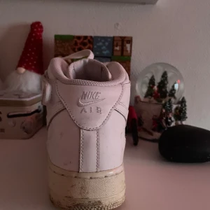 Nike Air Force 1 High vita sneakers - Nike Air Force 1 High sneakers i helvitt skinn med klassisk snörning och kardborreband runt ankeln. Snygg, chunky sula med cirkulärt mönster undertill och perforerad tå för extra ventilation. Ikonisk Swoosh-logga på sidan och AIR-detalj på mellansulan.