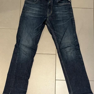 Replay mörkblå jeansbyxor 12A - Snygga mörkblå jeansbyxor från Replay med klassisk femficksdesign och gul kontrastsöm på bakfickorna. Modellen har rak passform och är tillverkad i slitstarkt denimtyg. Perfekt för dig som gillar stilrena och tidlösa jeans.