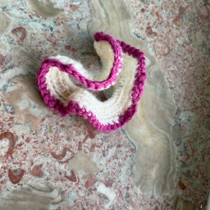 Handvirkat scrunshies - Unikt handvirkat scrunshie  i mjuk ull, med vågig form och kontrastkant i rosa. Basen är krämvit och armbandet har en cool, lekfull vibe som sticker ut. Perfekt för dig som gillar färg. 