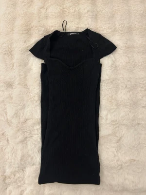 Svart ribbad klänning Gina Tricot XS - Supersnygg svart ribbad klänning från Gina Tricot i figurnära modell. Klänningen har korta ärmar, markerad byst och en söt hjärtformad urringning. Perfekt för dig som gillar en stilren och enkel look med lite edge.